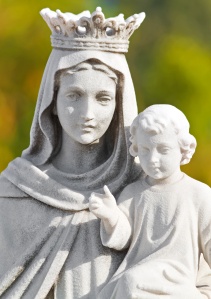 Crowned statue of the virgin Mary carrying a child with a diffused vegetation background